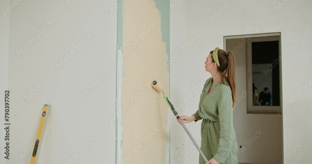 Young happy woman painting interior wall with paint roller in new house, Home decoration concept. Woman paints the wall. Portrait of a young woman making repairing in apartment. Painting new house Young happy woman painting interior wall with paint roller in new house, Home decoration concept. Woman paints the wall. Portrait of a young woman making repairing in apartment. Painting new house