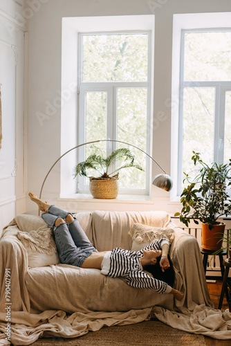 Relaxed woman lying on sofa in a cozy room with plants, by the window.