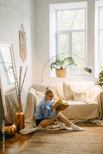 Young happy woman sitting on the floor at home in the morning with a book and coffee.