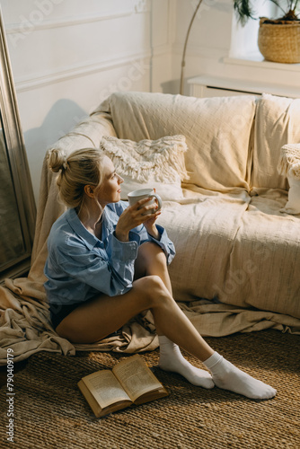 Young woman sitting on the floor at home in the morning with a book and coffee.