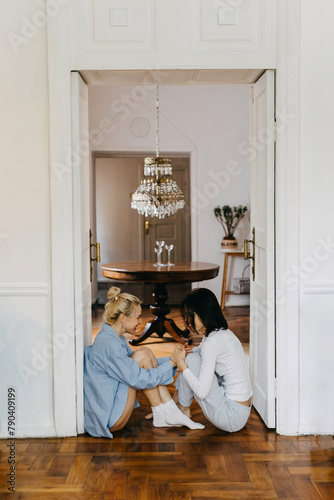 Two women, best friends, sitting at home on the floor, laughing, having a fun conversation.