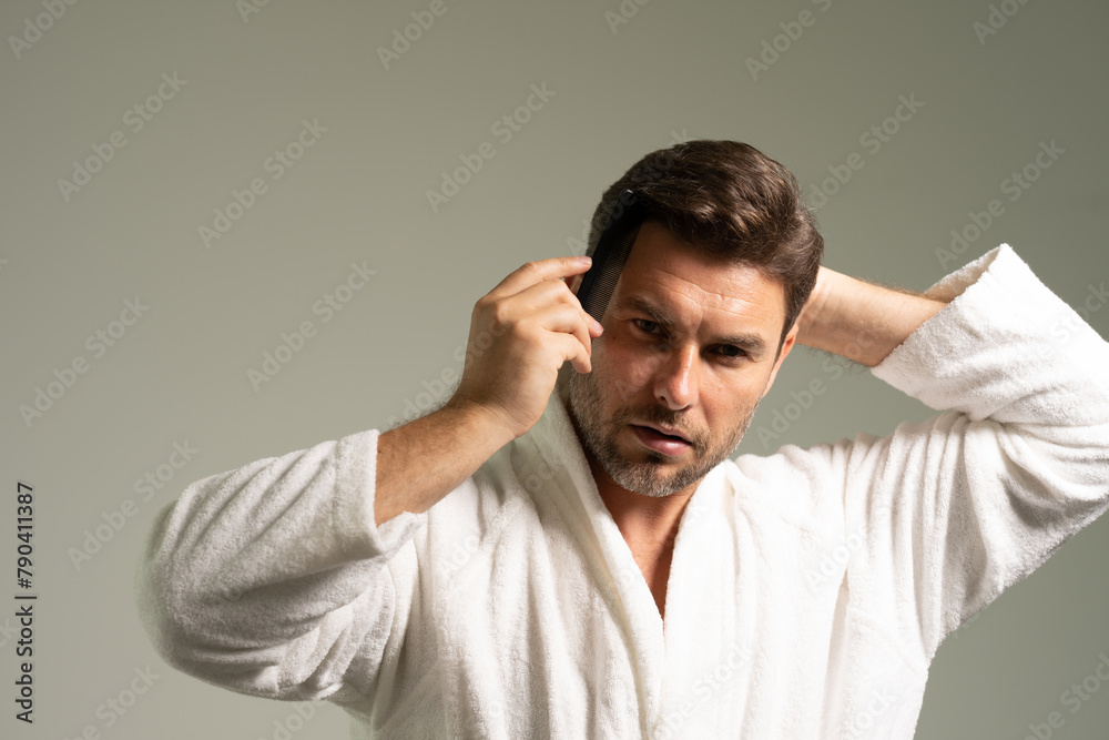 Happy handsome young shirtless man combing smooth straight hair, looking in mirror, enjoying beauty care activity, satisfied with haircare cosmetic products, haircut, barber work result Happy handsome young shirtless man combing smooth straight hair, looking in mirror, enjoying beauty care activity, satisfied with haircare cosmetic products, haircut, barber work result