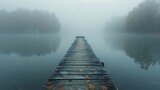 A solitary figure stands at the end of the weathered wooden pier, gazing into the mist-shrouded expanse of the serene lake.