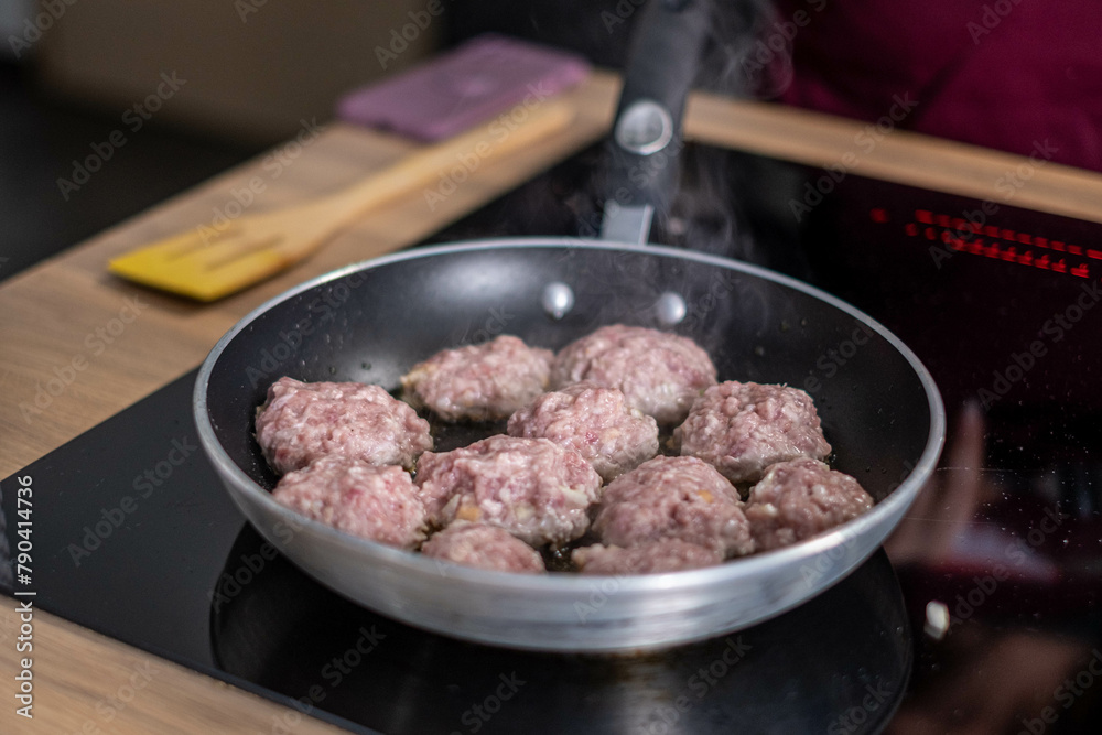 Steam wafts from juicy meatballs browning in a modern non stick frying pan, a scene of active cooking that speaks to homemade meal enthusiasts.
