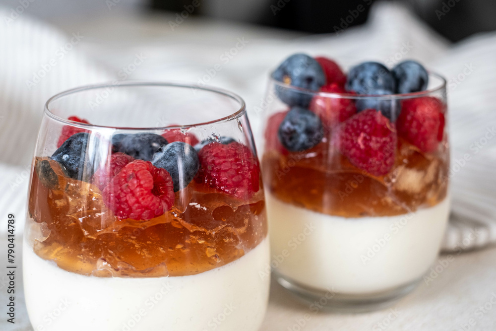 A single serving of berry parfait in focus, featuring a luscious layer of fruit jelly and crowned with a mix of berries, set against a soft, textile backdrop, a homestyle charm. A single serving of berry parfait in focus, featuring a luscious layer of fruit jelly and crowned with a mix of berries, set against a soft, textile backdrop, a homestyle charm.