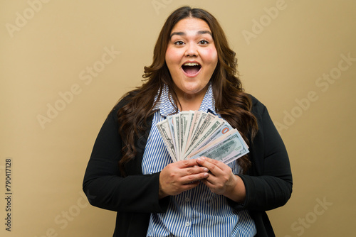 Joyful plus-size woman holding a fan of cash in the studio photo