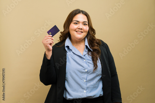 Cute plus-size businesswoman proudly displaying a credit card in a studio setting