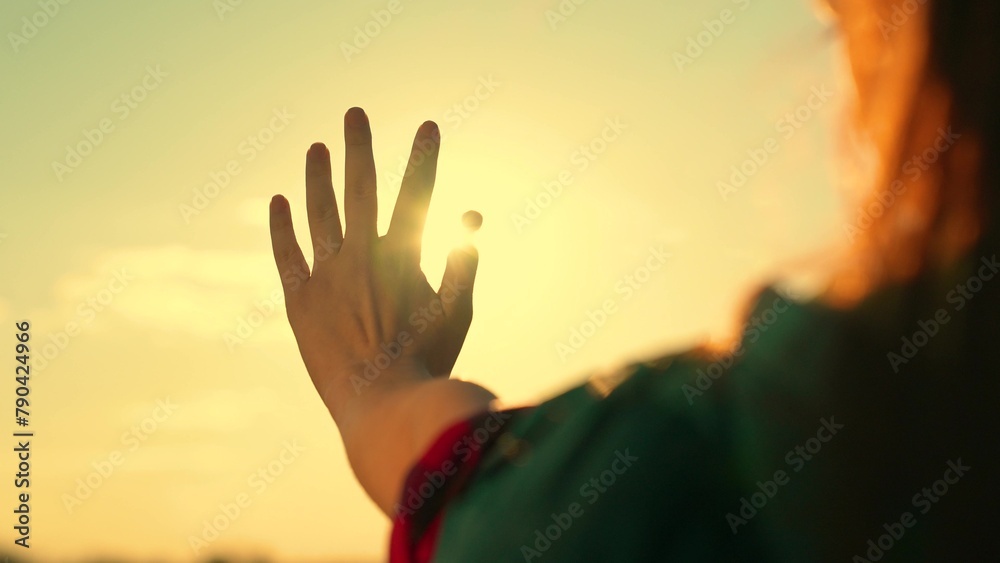 Happy teenage girl touches sun with her fingers. Child holds out his hand at sunset. Hand of happy young girl plays with glare of sun. Sunrise between fingers of child, teenager. Dream traveler, sky