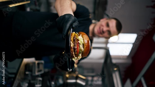 vertical video close up kitchen of the establishment examines in his hands a ready-made burger lying on a black plate photo