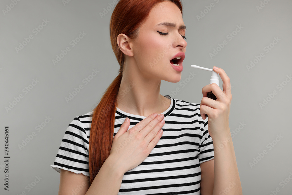 Young woman using throat spray on grey background Young woman using throat spray on grey background