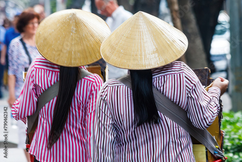 2 women walking down a street in Hanoi, Vietnam wearing conical hats photo
