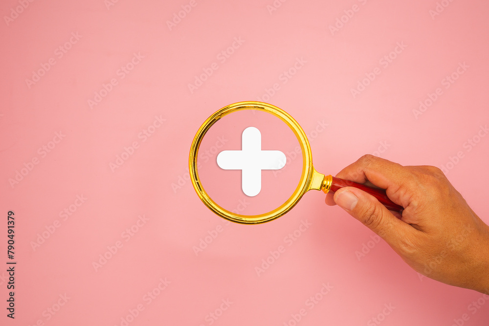 Hand holding a magnifying glass against a light pink background with a white plus symbol. Hand holding a magnifying glass against a light pink background with a white plus symbol.