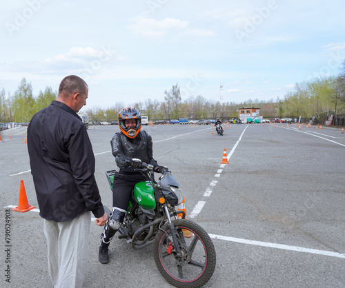 A young woman is learning to ride a motorbike in a motorcycle school. She is taught by a teacher