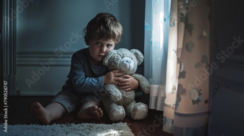 A small boy in a dark corner of a room, clutching a stuffed animal for comfort