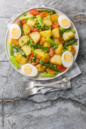 Fried potatoes with asparagus, cherry tomatoes, egg and green peas close-up in a plate on the table. Vertical top view from above