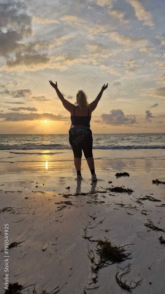 Frau mit Glück und Freude bei Sonnenaufgang am Strand mit Händen nach oben