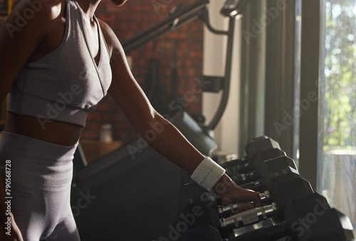 Woman, fitness and weightlifting with dumbbell at gym for workout, training or indoor exercise. Active female person or hands with small weights by rack for strength or muscle gain at health club © peopleimages.com