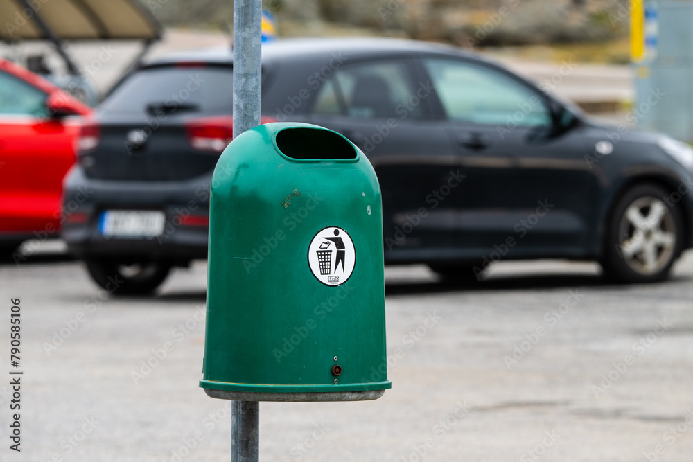 Green round plastic trash can by a parking lot. Green round plastic trash can by a parking lot.