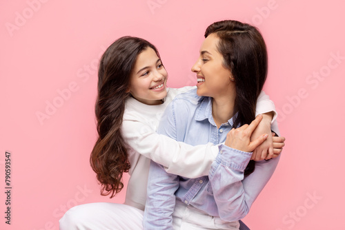 Happy woman posing with her pretty preteen daughter, having fun and smiling, posing on pink color studio background. Mother's Day