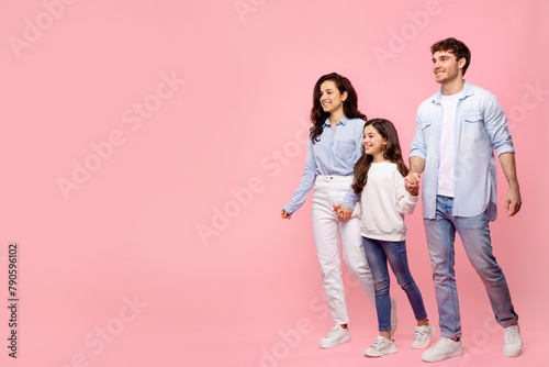 Young happy parents with daughter in casual clothes hold hands walking, going strolling isolated on pastel pink background, free copy space