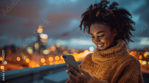 A smiling woman of color looking at their phone illuminating her face, standing outside at dusk. a city skyline is far in the distance. Generative AI. photo