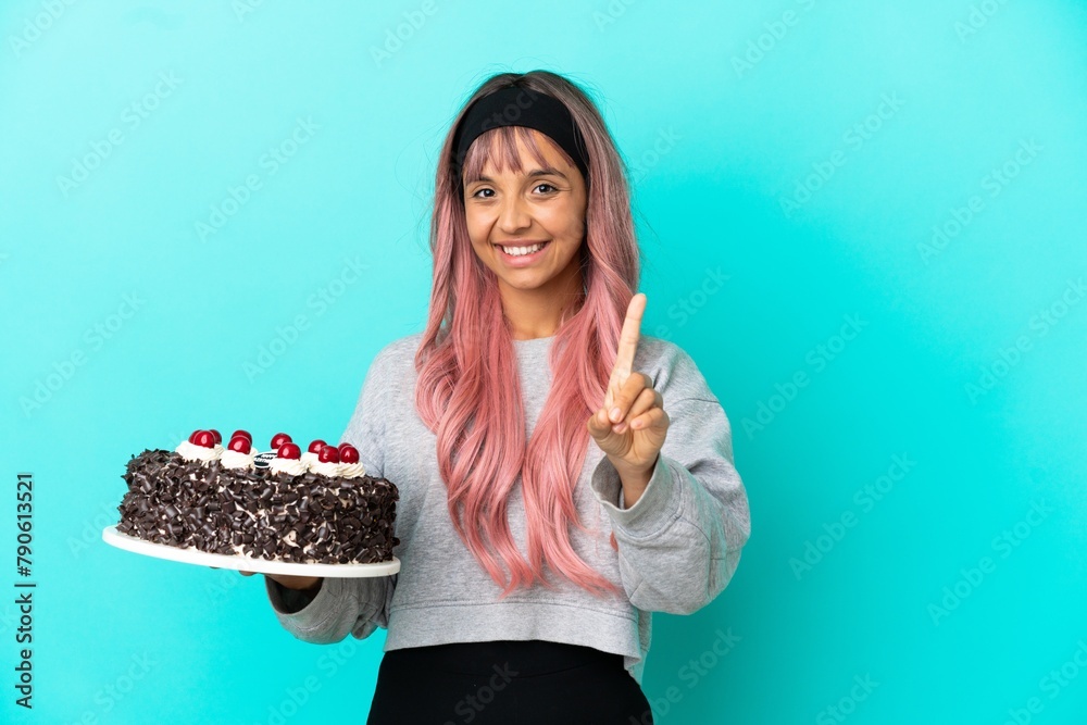 Young woman with pink hair holding birthday cake isolated on blue background showing and lifting a finger Young woman with pink hair holding birthday cake isolated on blue background showing and lifting a finger