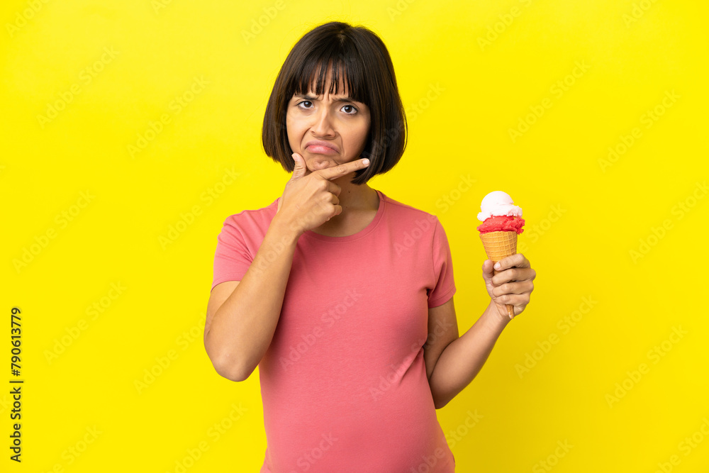 Pregnant woman holding a cornet ice cream isolated on yellow background thinking