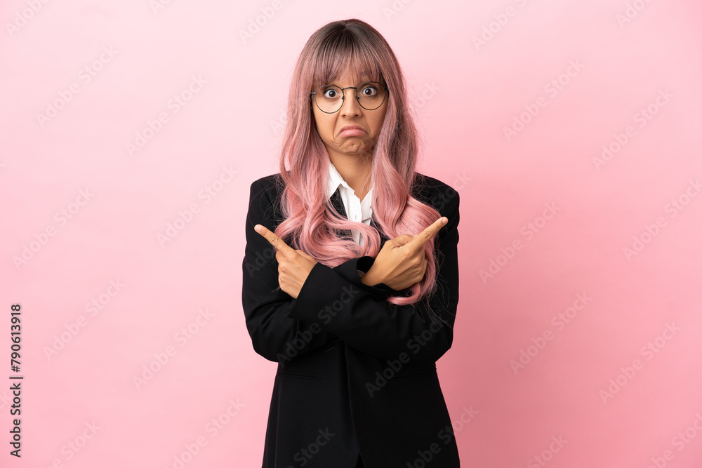 Young business mixed race woman with pink hair isolated on pink background pointing to the laterals having doubts Young business mixed race woman with pink hair isolated on pink background pointing to the laterals having doubts