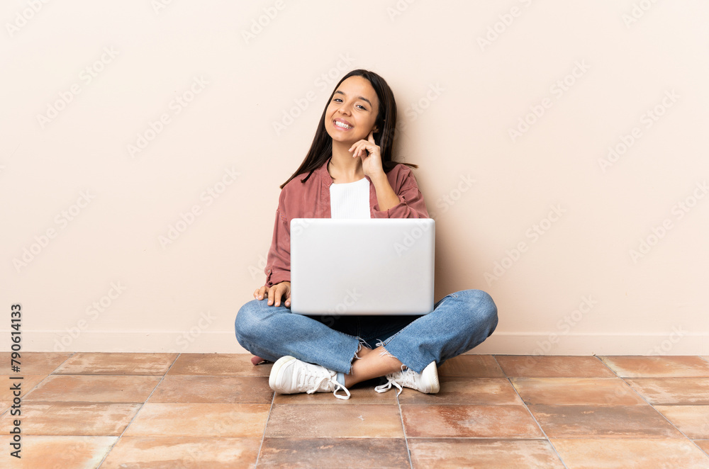 Young mixed race woman with a laptop sitting on the floor laughing Young mixed race woman with a laptop sitting on the floor laughing