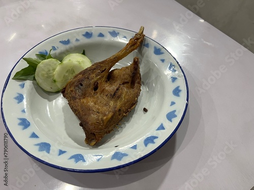 Indonesian traditional deep fried duck thigh and leg served on a plate with slices of cucumber and basil leaves