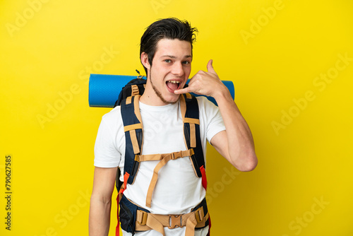 Young mountaineer Russian man with a big backpack isolated on yellow background making phone gesture. Call me back sign