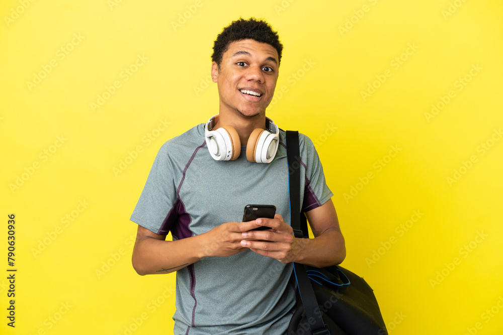 Young sport African American man with sport bag isolated on yellow background surprised and sending a message Young sport African American man with sport bag isolated on yellow background surprised and sending a message