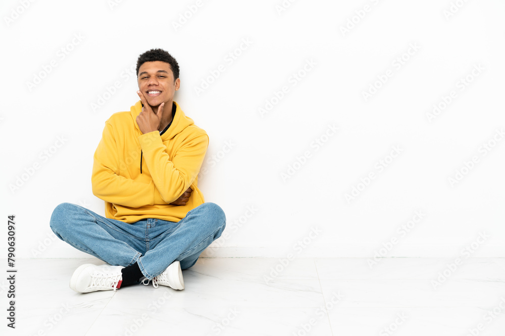 Young African American man sitting on the floor isolated on white background smiling