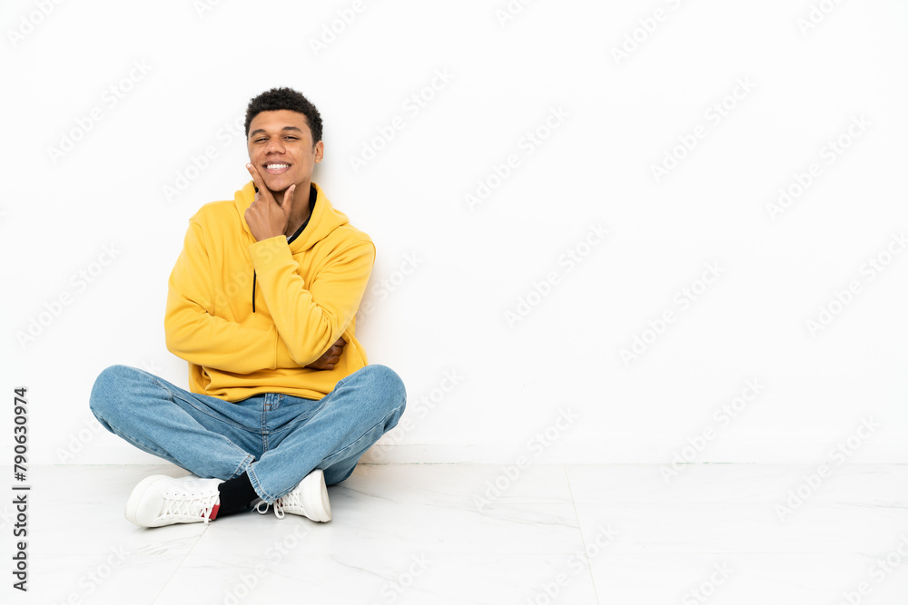 Young African American man sitting on the floor isolated on white background smiling Young African American man sitting on the floor isolated on white background smiling