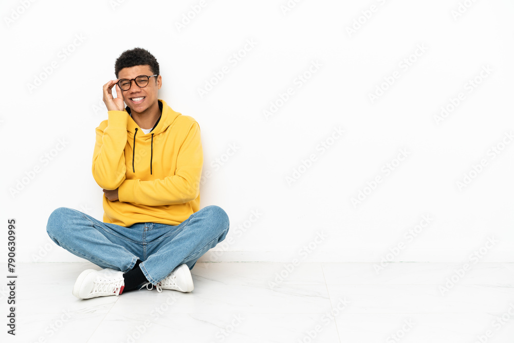 Young African American man sitting on the floor isolated on white background with glasses and happy Young African American man sitting on the floor isolated on white background with glasses and happy