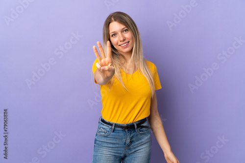 Young blonde woman isolated on purple background happy and counting three with fingers