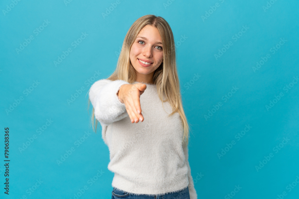 Young blonde woman isolated on blue background shaking hands for closing a good deal