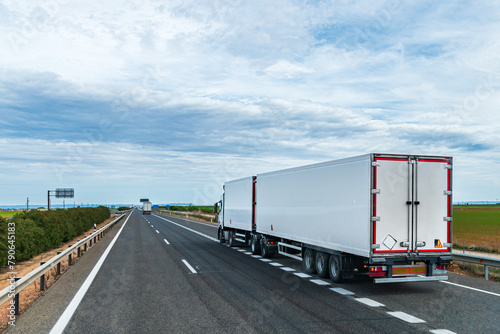 Truck with two refrigerated semi-trailers joining a highway, new sizes of vehicles called Duo-trailer, rear side view.