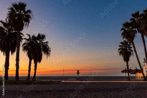 Fototapeta Naklejka Na Ścianę i Meble -  Sunrise on Poniente beach, Motril, Granada, with palm trees, a beach bar and a watchtower for bathers, Tropical coast.