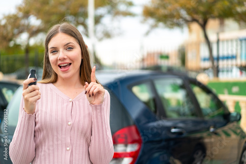 Young pretty blonde woman holding car keys at outdoors pointing up a great idea