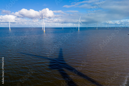 A vast body of water glistens under the spring sunlight as wind turbines stand tall in the background, harnessing the power of the wind © Fokke Baarssen