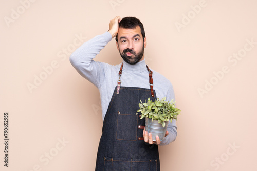 Man holding a plant over isolated background with an expression of frustration and not understanding