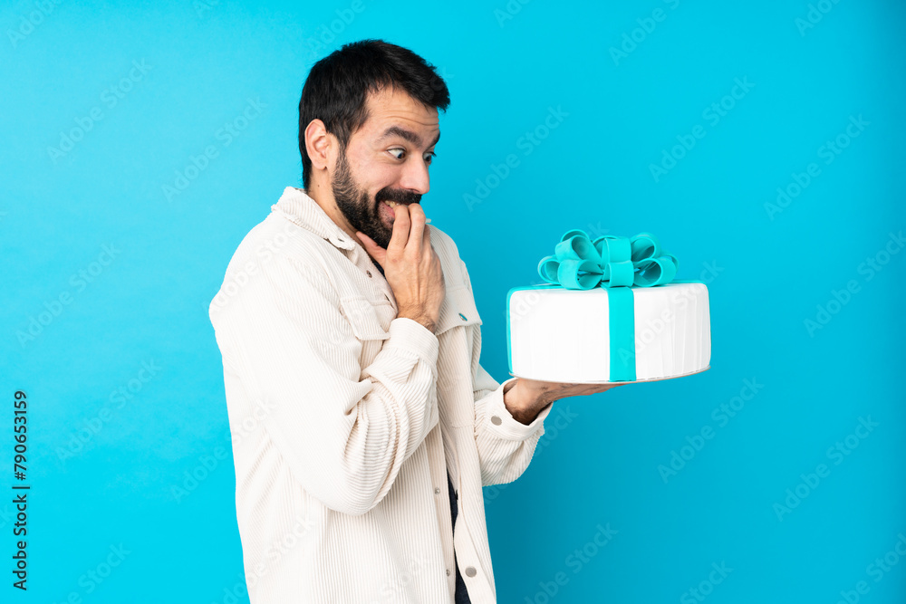 Young handsome man with a big cake over isolated blue background