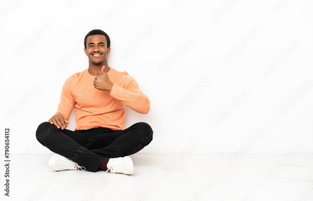 African American man sitting on the floor over isolated copyspace background giving a thumbs up gesture African American man sitting on the floor over isolated copyspace background giving a thumbs up gesture