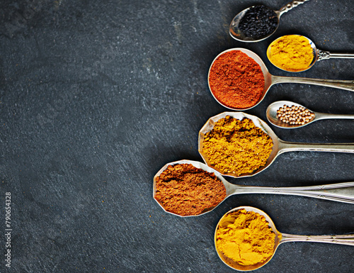 Spoon, powder and group of spices by dark background for cooking dinner, health and nutrition. Turmeric, chilli and seeds on black surface with zoom for Oriental food, antioxidant and spicy cuisine
