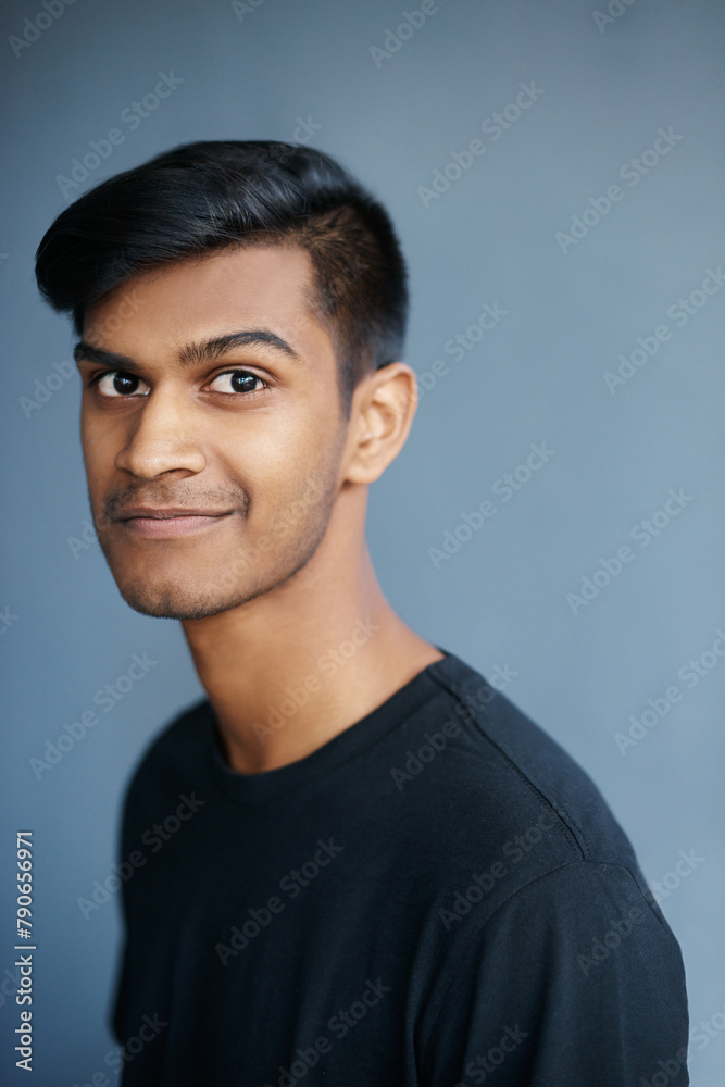 Fototapeta premium Young, Indian and man in portrait with smile, confident and proud with student isolated on blue background. Casual, tshirt and positive with gen z for college, cool and calm with model in studio