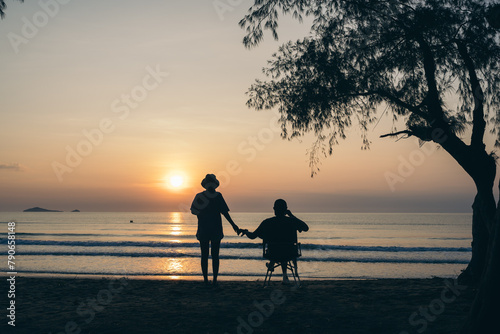 Tourist couple on the beach under the tree and watch the sunrise, colorful golden morning light, Outdoor lifestyle concept.
