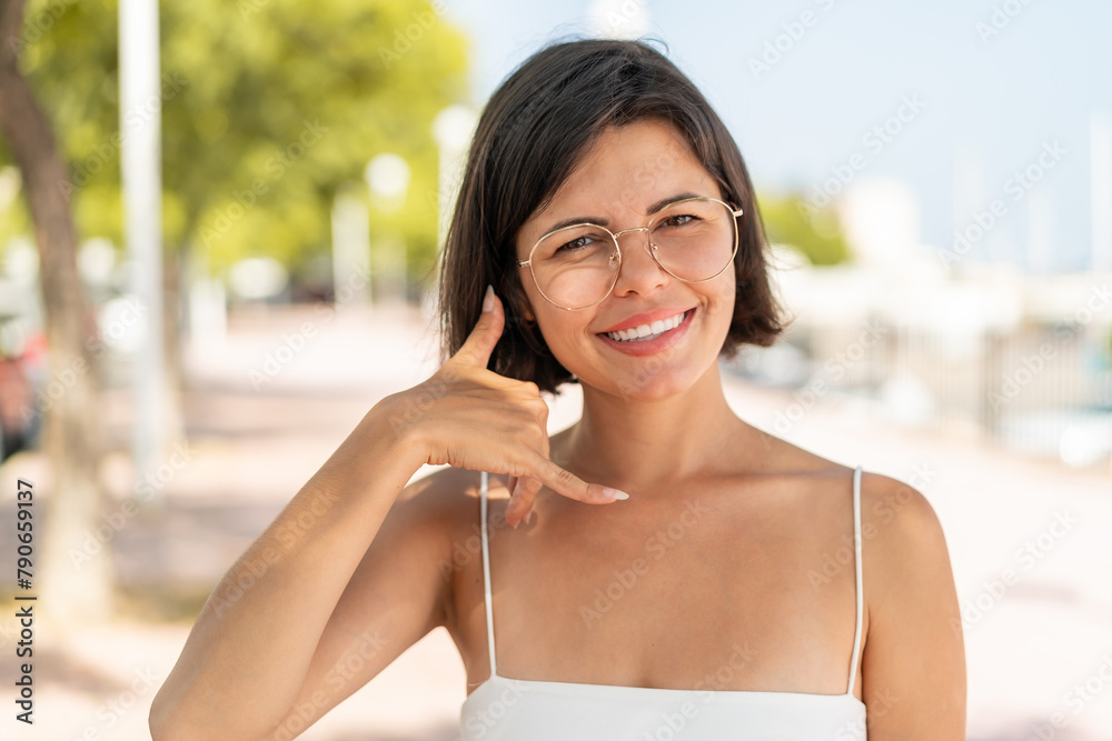 Young pretty Bulgarian woman with glasses at outdoors making phone gesture. Call me back sign