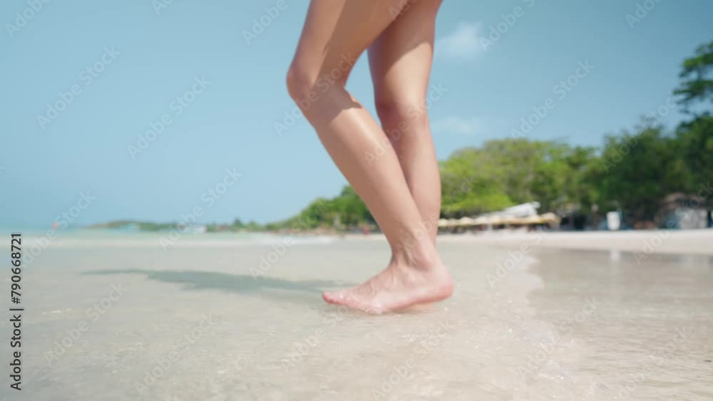Close Up shot of young female beautiful legs slowly kicking a hit low tide wave while standing playing alone on a quite white sea sand beach during sunny day. female body care. Travel Nature Concept Close Up shot of young female beautiful legs slowly kicking a hit low tide wave while standing playing alone on a quite white sea sand beach during sunny day. female body care. Travel Nature Concept