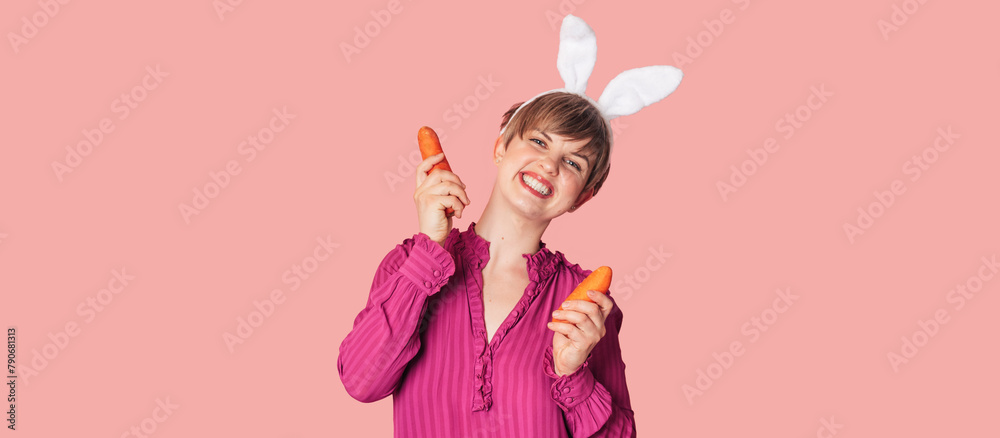 Smiling slender Caucasian girl in bunny ears with fresh carrots in her hands. Panoramic banner, free space. Organic vegetables.